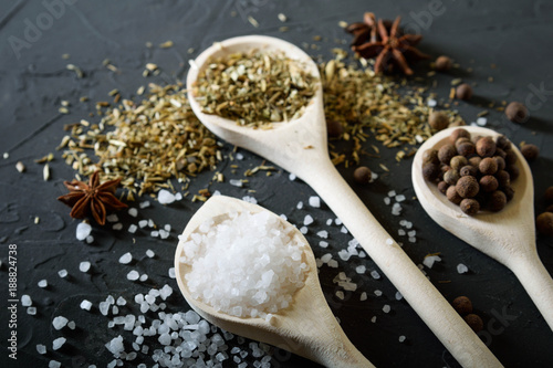  Wooden spoon with Italian seasoning-dried oregano with thyme  basil and vegetables.Oregano in a wooden spoon on a rocky concrete dark black background with a place for text.Top view.salt crystals pep