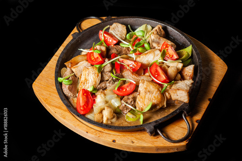 Pieces of meat fried on pan with vegetables on black background