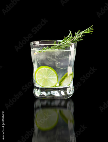 Vodka, lime wedge with ice in rocks glass on black background with reflection
