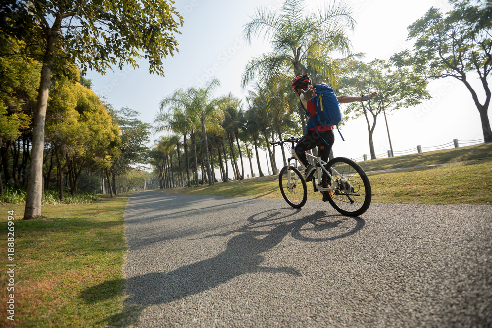 woman cyclist riding bike with outstretched arms in tropical park