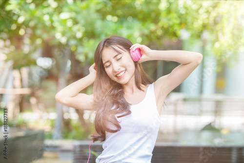 Happy young beautiful girl listening to the music with her pink headphones and dancing in the urban park