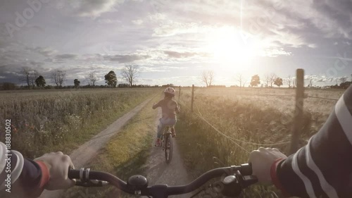 Little girl riding bicycle on rural road. Summer lifestyle moment of a happy childhood.