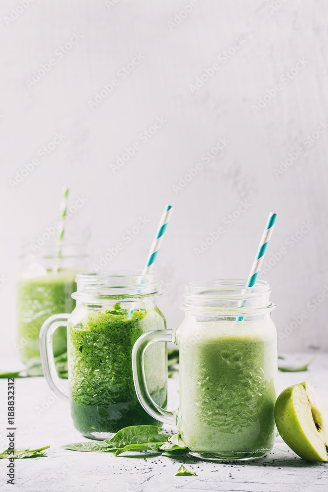 Variety of three color green spinach kale apple yogurt smoothie in mason jars with retro cocktail tubes over gray background. Healthy vegan detox eating. Toned image Variety of three color green spinach kale apple yogurt smoothie in mason jars with retro cocktail tubes over gray background. Healthy vegan detox eating. Toned image