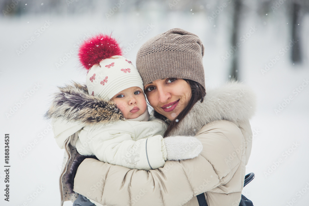 Close up brunette young women portrait with baby girl, daughter hugs and smiling in snowy park.