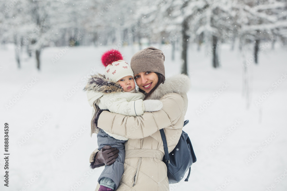 Brunette young women portrait with baby girl, daughter hugs and smiling in snowy park.