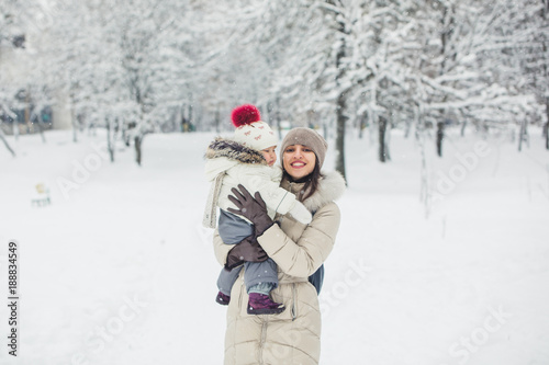 Brunette young women portrait with baby girl, daughter hugs and smiling in snowy park.