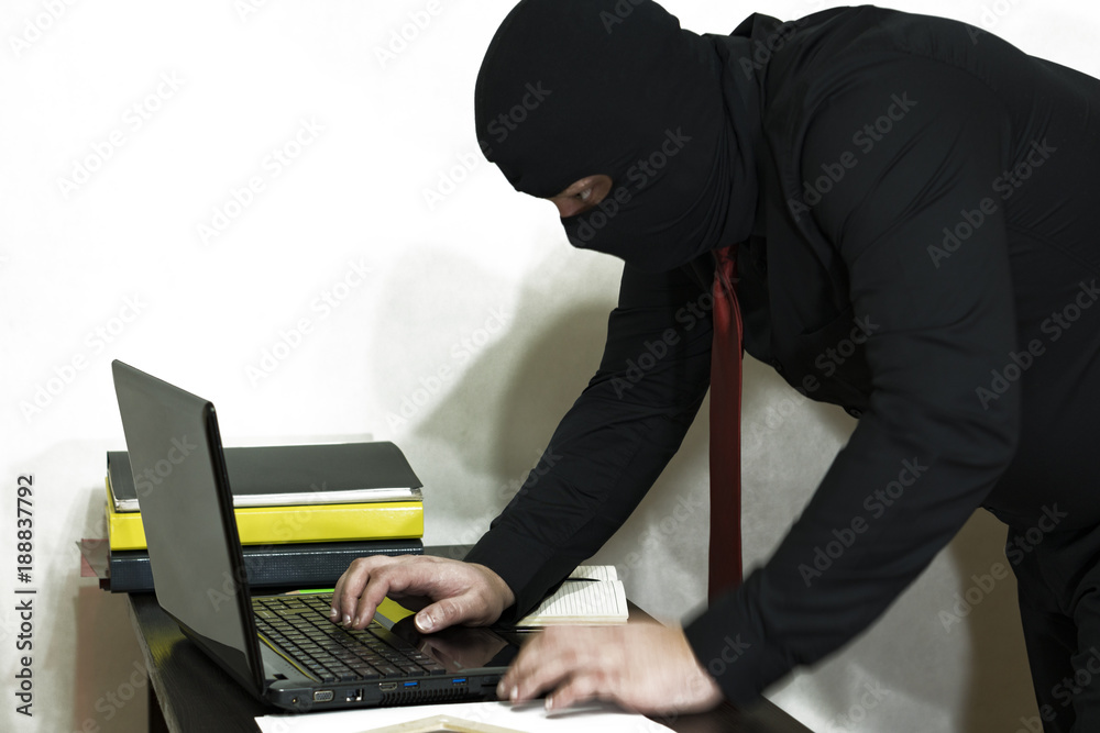 Electronic burglar in the balaclava. Performs hacking of the computer. Receipt of classified information. Side view. computer crime Electronic burglar in the balaclava. Performs hacking of the computer. Receipt of classified information. Side view. computer crime