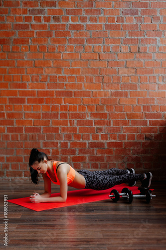 Young, fit and sporty woman in leggings and top in front of brick white wall. The woman trains an abdominal tension. Fitness, sport lifestyle concept.