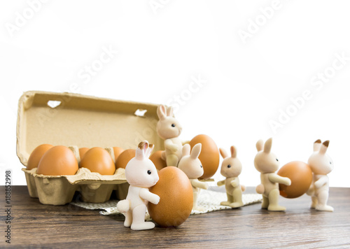 Rabbit dolls are preparing to celebrate Easter.Rabbits are lifting eggs from paper crates to use in Easter on a white background on a wooden table.