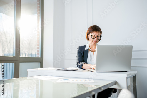 Elegant senior businesswoman dressed in the suit working with laptop at the white office