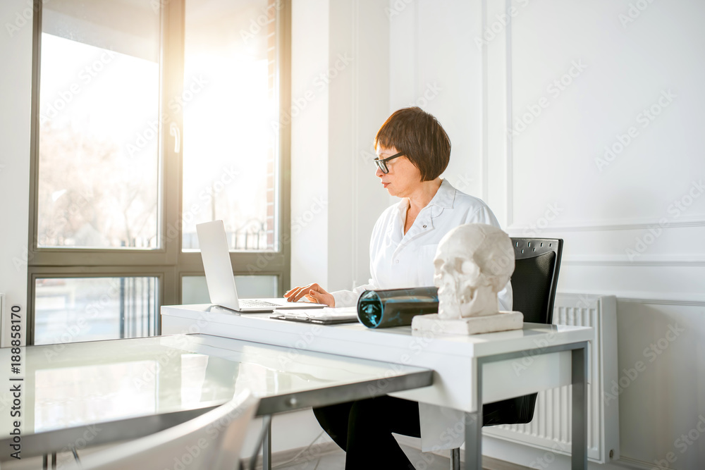 Portrait of a senior woman doctor working with laptop in the beautiful white office interior