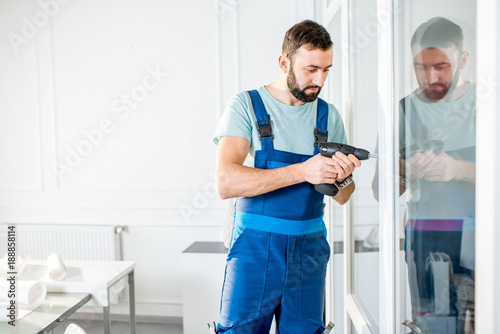 Repairman in the workwear drilling glass partition in the office