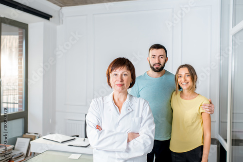Portrait of a senior woman doctor standing with young couple of patients in the white office
