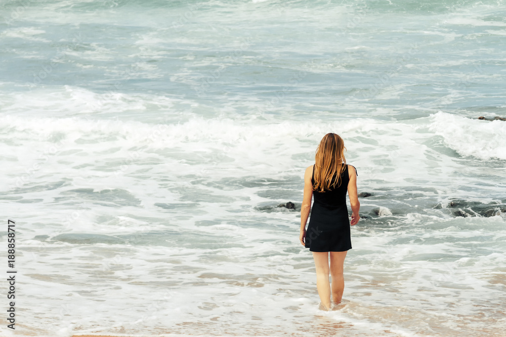 Woman with back view enters the sea wearing a dress