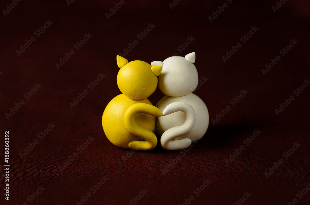 Two minimalistic animal figures in love. Lovely cat plasticine models having tails in heart shape isolated on dark red background. Happy Valentine's Day in minimalism style.