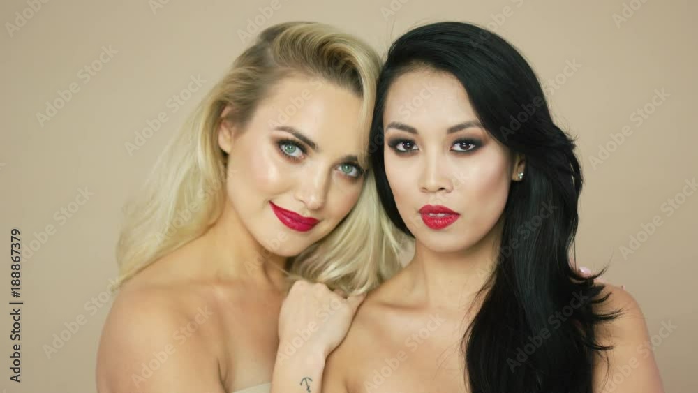 Studio portrait of two pretty cheerful female models with blonde and brunette hair looking at camera together.