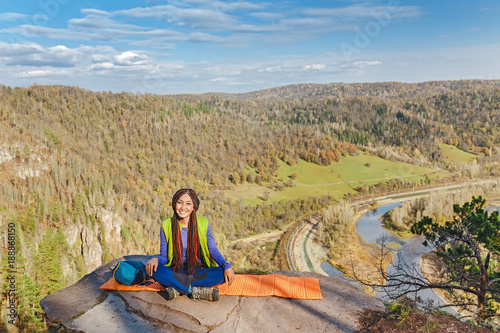 Young woman hiker sitting on cliff's edge at high mountain