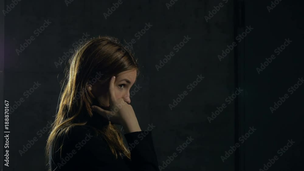 A portrait of a girl's face in profile as she makes thinking hand gestures and faces by putting her fingers to her temple. The girl is wearing a black dress and standing behind a grey wall. Medium clo A portrait of a girl's face in profile as she makes thinking hand gestures and faces by putting her fingers to her temple. The girl is wearing a black dress and standing behind a grey wall. Medium clo