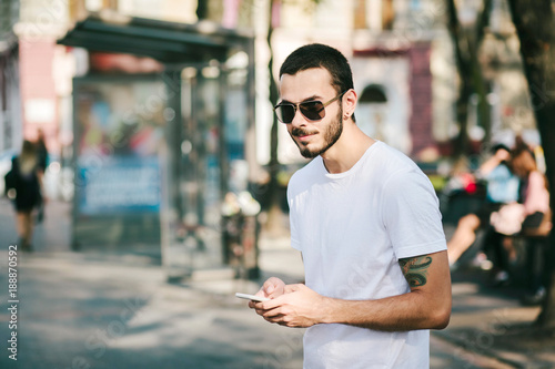 Half length portrait of bearded hipster man dressed in stylish clothes chatting on cell telephone while standing in the street use smart phone during strolling outdoors