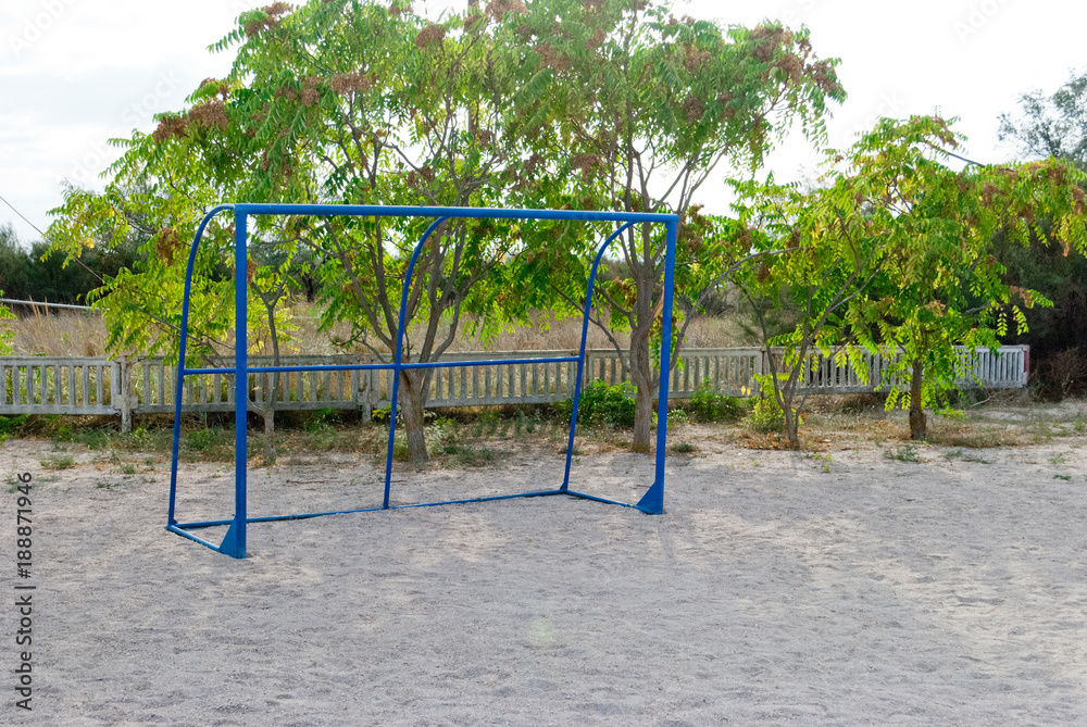 Fototapeta premium Blue football gate without mesh, stand on the sand, against the background of bushes trees, blue sky sun sports rest, playground, children's games