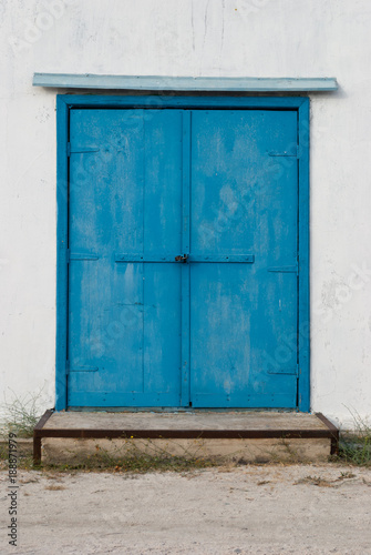 Old vintage blue metal door in a white wall, concrete foundation step, bolt lock, visor
