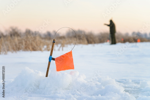 Winter fishing rod and ice hole close up, tip-up with reel and orange flag tackle.