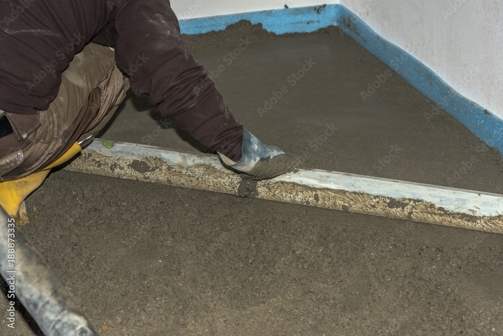 Screed flooring is processed in a residential building. A worker performs sand and cement screed floor over floor heating. Sand and cement floor screed. Concept: construction site and craft Screed flooring is processed in a residential building. A worker performs sand and cement screed floor over floor heating. Sand and cement floor screed. Concept: construction site and craft