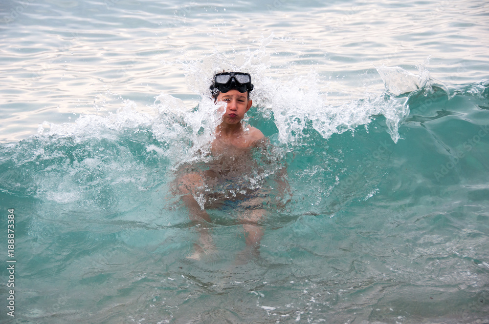 Young boy enjoying his summer vacation, swimming and playing in the sea with waves splashing over him  