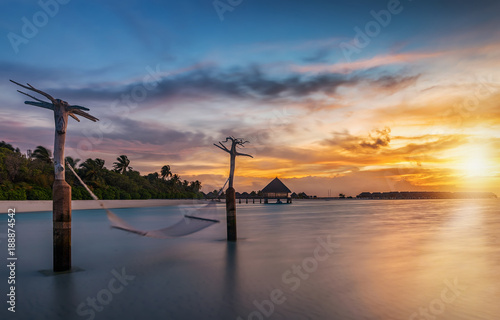 Sonnenuntergang hinter einer tropischen Insel mit Hängematte die im Wind schwingt photo