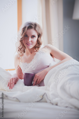 Young woman drinking cup of coffee or tea while lying in bed. © lenets_tan