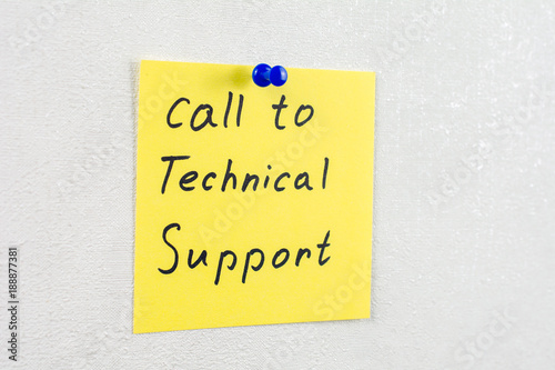 call to technical support note reminder yellow sticker on a white wall pinned with blue pushpin, close up, selective focus