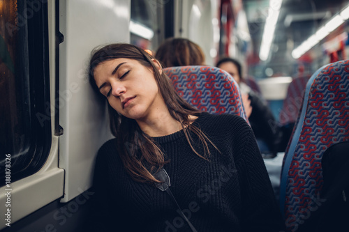 Passenger woman sitting in her seat and sleeping inside a train/bus while traveling.Tired exhausted woman taking a nap in public transportation.Falling asleep during a long ride.