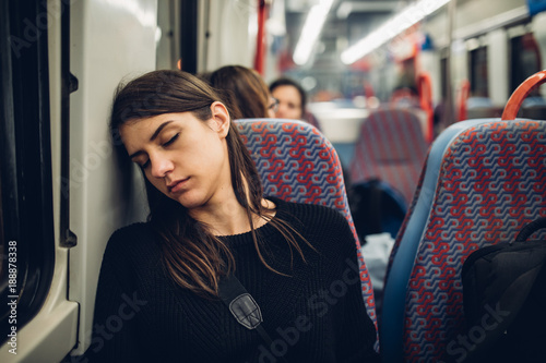 Passenger woman sitting in her seat and sleeping inside a train/bus while traveling.Tired exhausted woman taking a nap in public transportation.Falling asleep during a long ride. photo