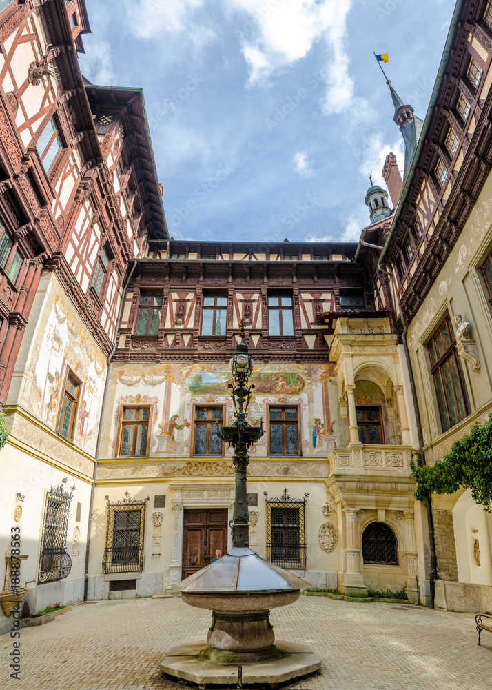 Wide interior courtyard view from the Peles Castle in Romania with beautiful mural paintings, stone and wood details on the walls a sunny bright day