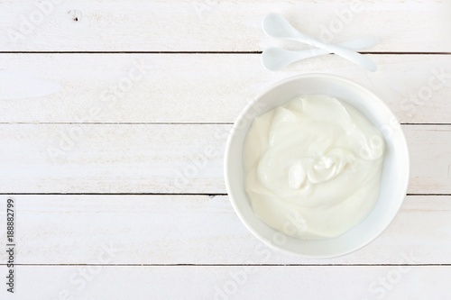 Greek yogurt in a white bowl, above view a white wood background