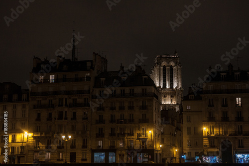 Notre Dame de Paris cathedral surrounded by medieval residential buildings typical from Ile de la Cite in Paris, France, during an winter evening, taken from the quays of Seine river..
