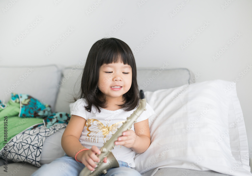 Little asian girl with saxophone toy in living room.