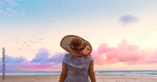 Relaxing woman sitting on the beach looking at sea and sky with hat. Dream travel and vacation concept. Can be used for banner