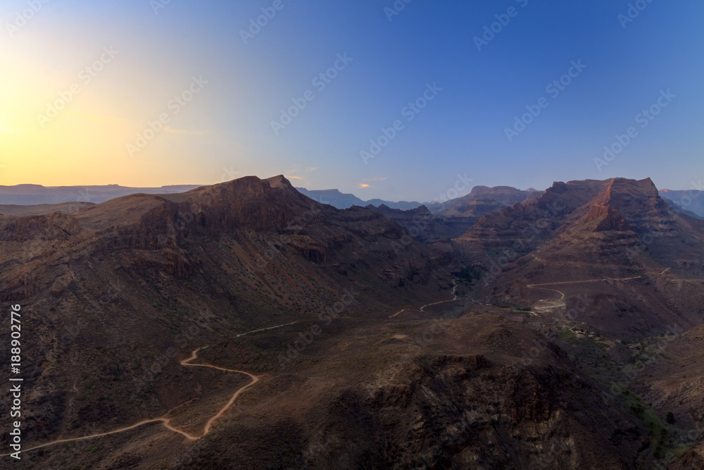 Sunset above mountains and canyon with rural road on bottom.