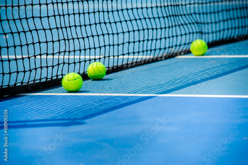 tennis balls on front of blue hard court with black net © OHishi_Foto