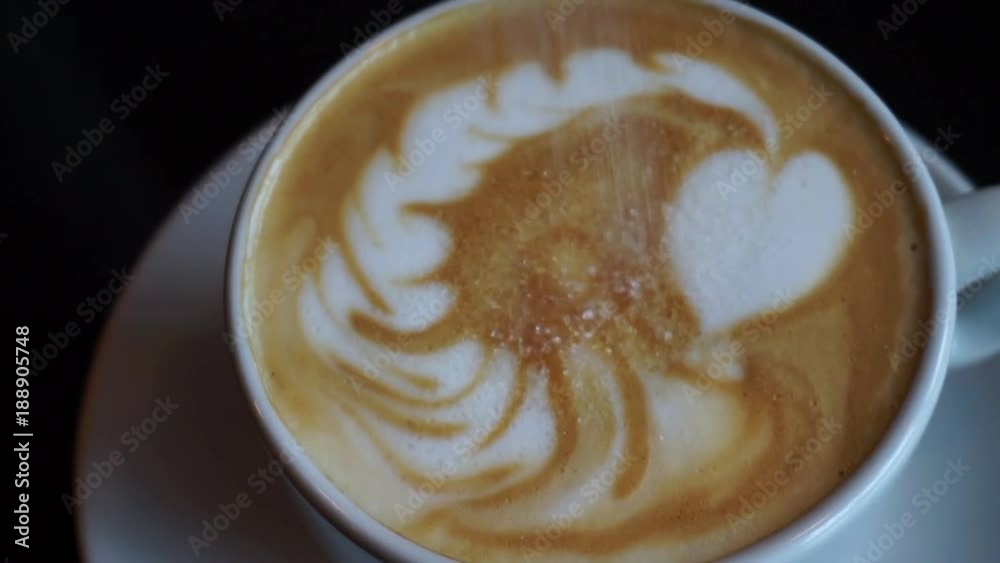 White sugar falling over cappuccino milk foam and dissolving White sugar falling over cappuccino milk foam and dissolving
