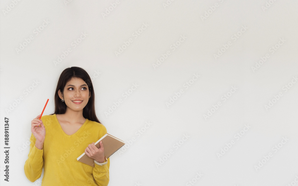 Happy young student woman holding pencil and book with smiling against a white wall background, education back to school concept Happy young student woman holding pencil and book with smiling against a white wall background, education back to school concept