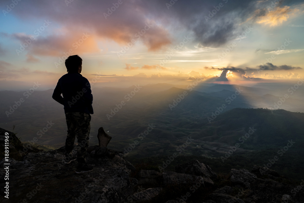 Young man hiker relaxing on top of a mountain at sunset
