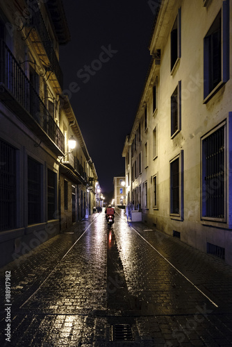 Motorcyclist passing through the street called "Pedro Gumiel" in Alcala de Henares, Madrid, Spain, on a very rainy and cold December night with beautiful reflections of water on the cobblestones of © peizais