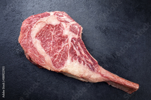 Raw dry aged wagyu tomahawk steak as close-up on black board