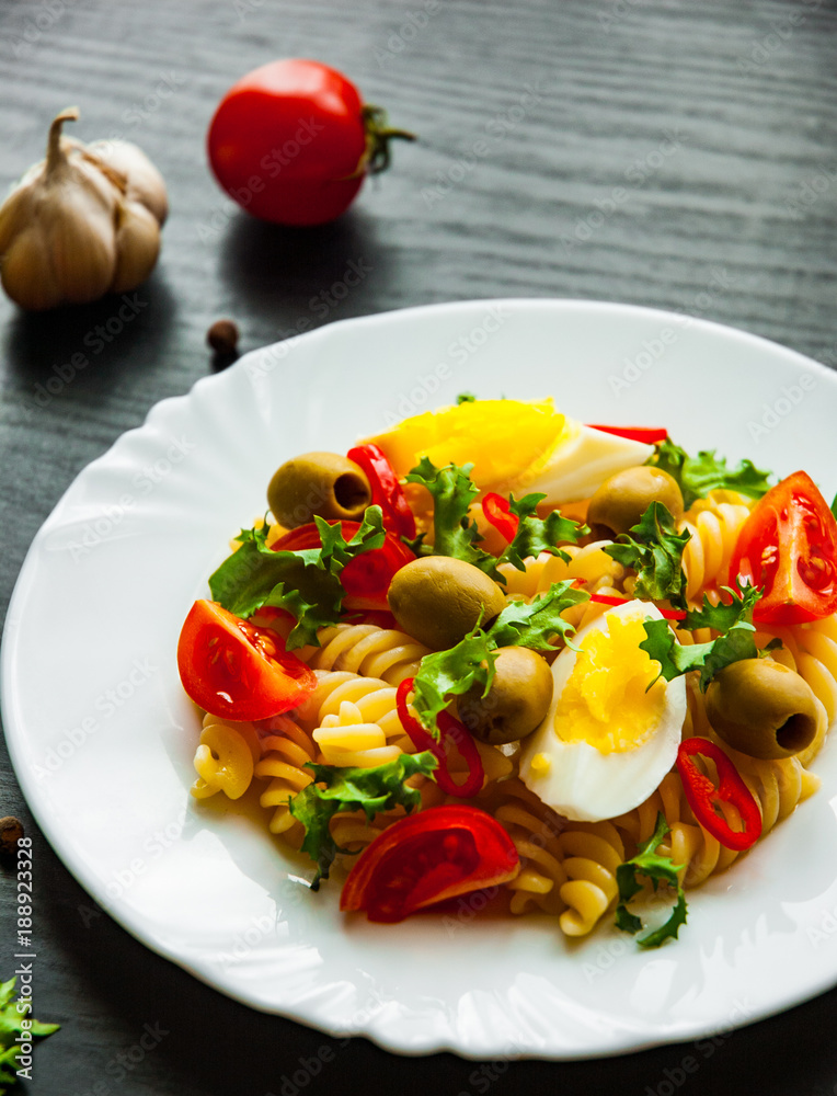 fusilli pasta salad with tomato, eggs and olive in plate on dark wooden background fusilli pasta salad with tomato, eggs and olive in plate on dark wooden background