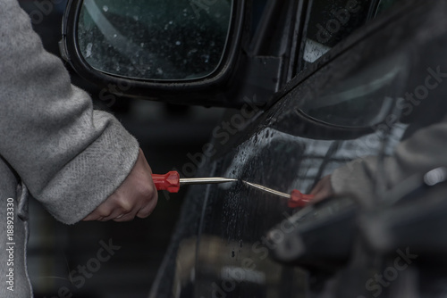 A woman holds a screwdriver in her hand and wants to scratch the car paint. She retaliates from jealousy. Concept: vandalism and crime