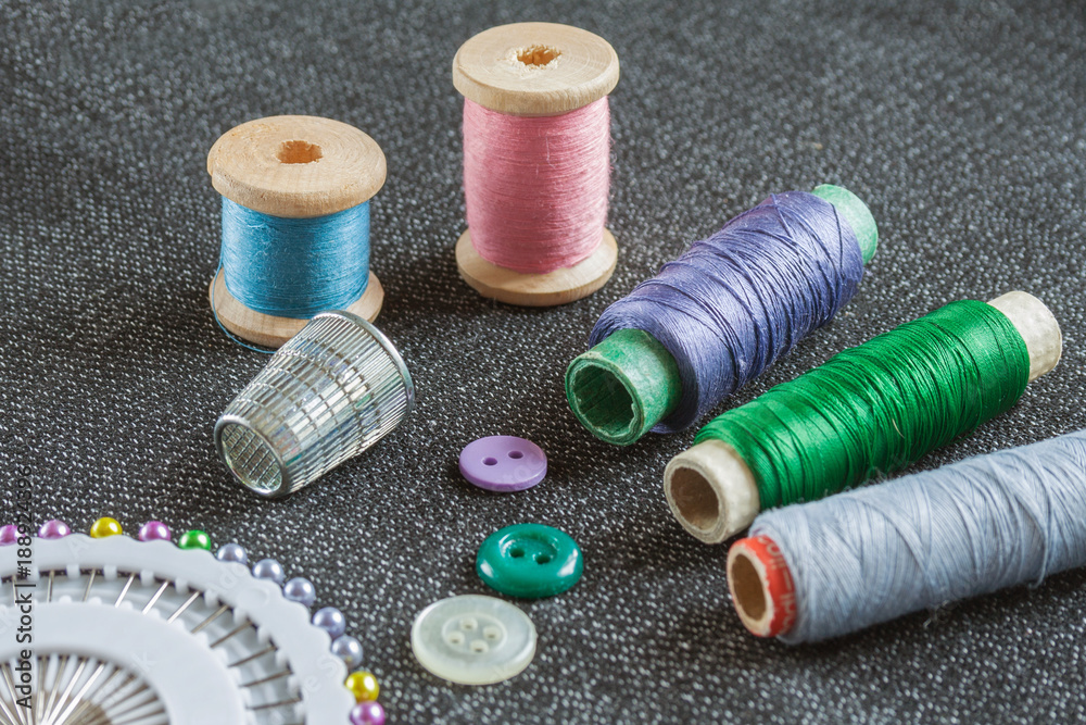 Sewing accessories: spools of threads, needles, thimble, buttons on the textured fabric surface Sewing accessories: spools of threads, needles, thimble, buttons on the textured fabric surface