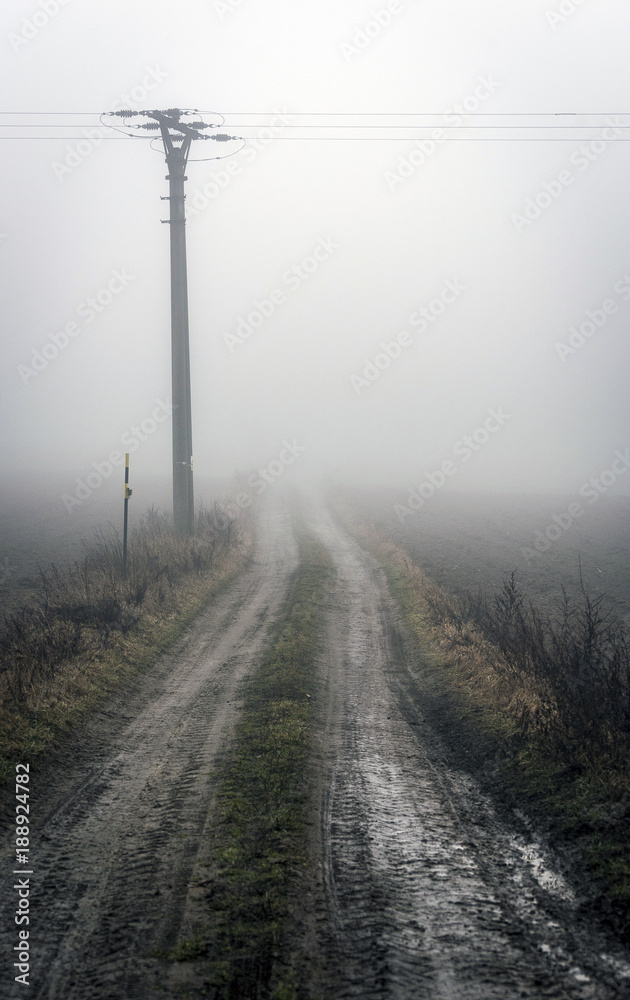 a column with an electric line on a muddy field path emerging from the mist in the highlands a column with an electric line on a muddy field path emerging from the mist in the highlands