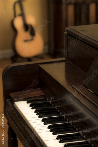 Old vintage wooden upright piano, white ivory keys and acoustic guitar and antique radio in background